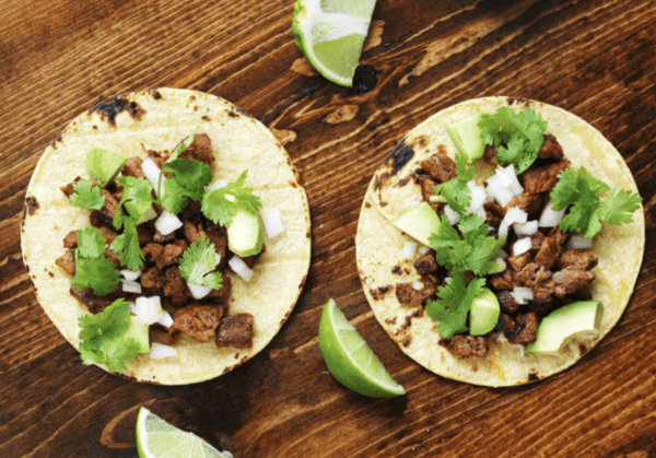 Two tacos with meat, avocado, and cilantro.